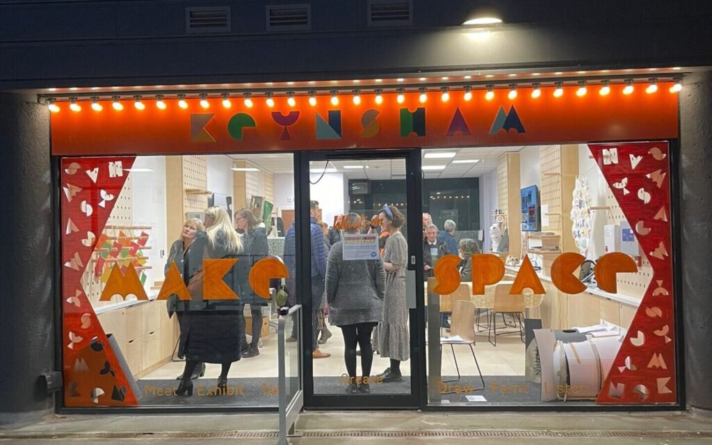 Image of a brightly lit orange shopfront. Inside is a group of people chatting.